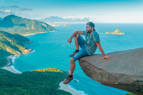 Imagem de homem sentado no pico da Pedra do Telégrafo, no Rio de Janeiro, após fazer a trilha que dá acesso ao local.