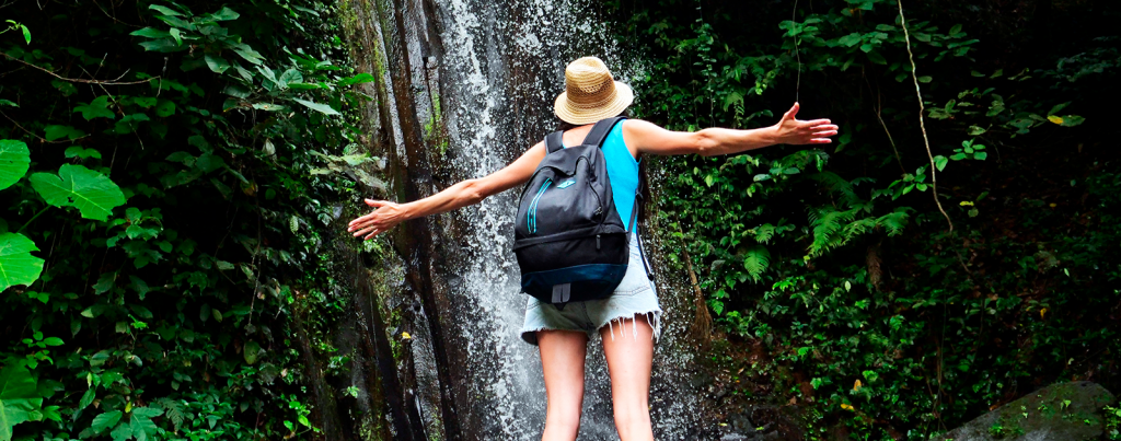 Imagem de uma mulher de costas olhando para a queda d’água de uma cachoeira.